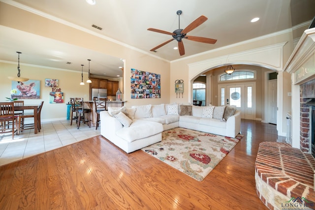 living room featuring ceiling fan, a fireplace, light hardwood / wood-style floors, and ornamental molding