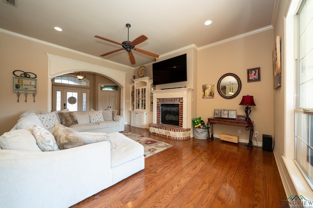 living room with hardwood / wood-style floors, a brick fireplace, ceiling fan, and ornamental molding