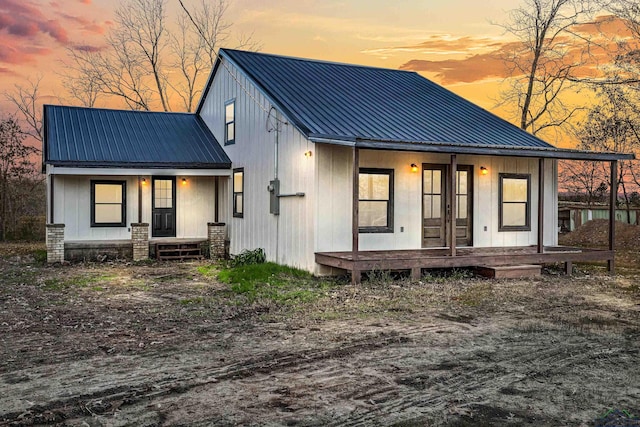 back house at dusk featuring covered porch and french doors