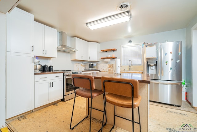 kitchen with wall chimney exhaust hood, white cabinetry, stainless steel appliances, sink, and a breakfast bar area