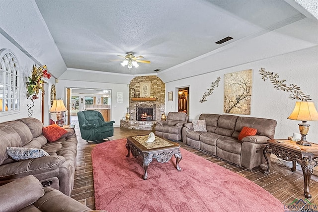 living room with lofted ceiling, a stone fireplace, ceiling fan, ornamental molding, and a textured ceiling