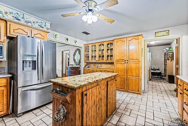 kitchen with stainless steel fridge with ice dispenser, a center island, a textured ceiling, and ceiling fan