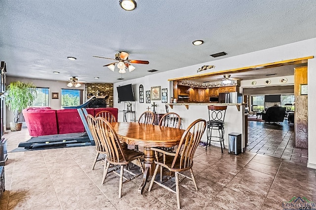 dining room featuring a fireplace, ceiling fan, and a textured ceiling