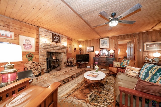 living area with wood ceiling, ceiling fan, wood walls, and a wood stove