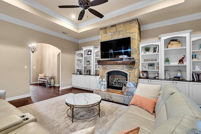 living room with ceiling fan, a raised ceiling, dark hardwood / wood-style floors, a fireplace, and ornamental molding