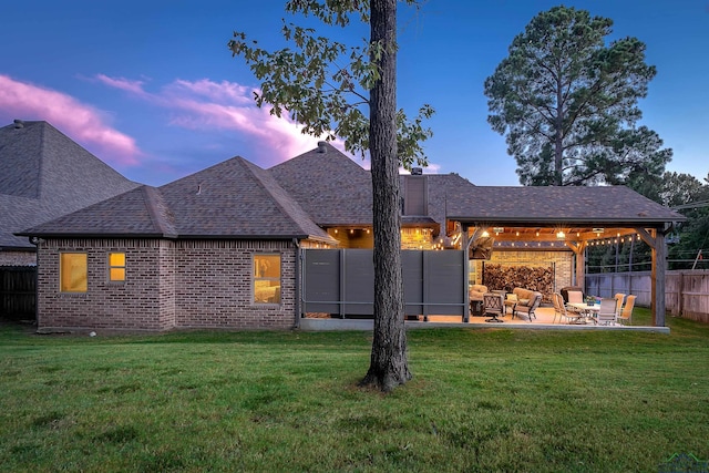 back house at dusk with a patio area and a yard