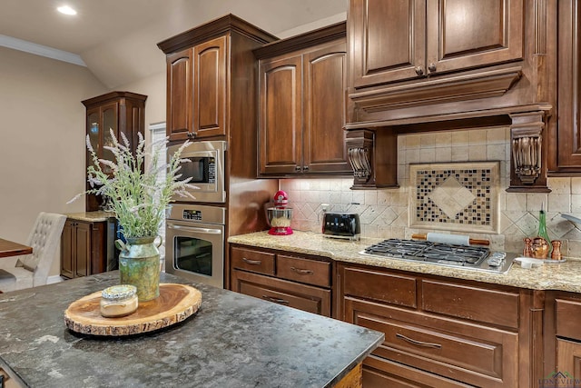 kitchen featuring tasteful backsplash, dark stone countertops, vaulted ceiling, appliances with stainless steel finishes, and custom exhaust hood