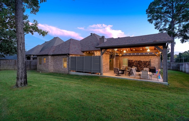 back house at dusk featuring a lawn and a patio area