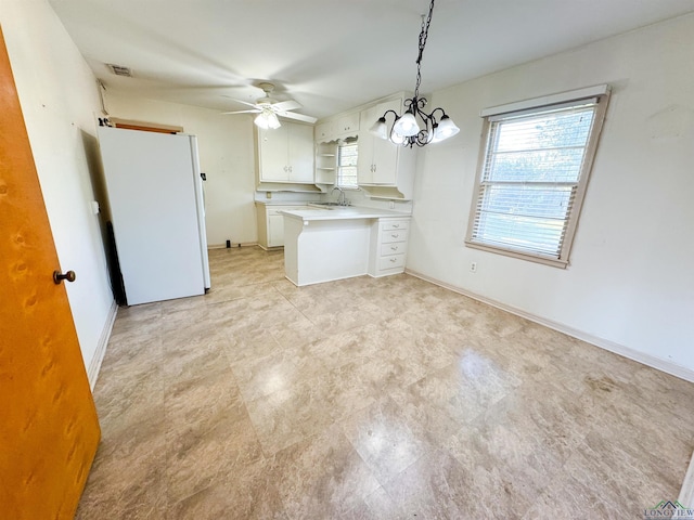 kitchen featuring sink, hanging light fixtures, white refrigerator, white cabinets, and ceiling fan with notable chandelier