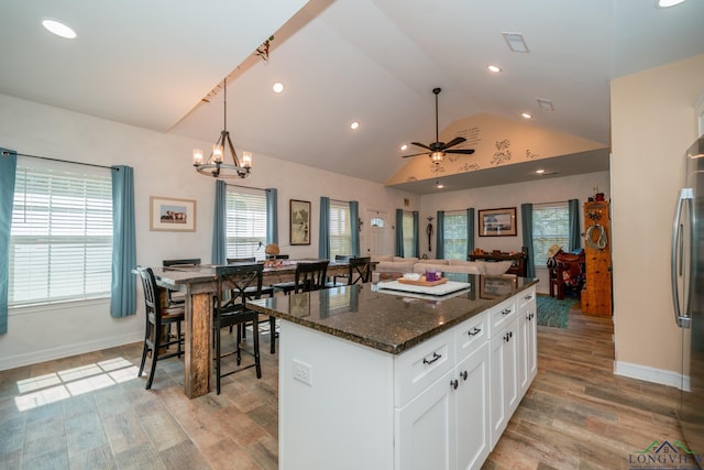 kitchen featuring lofted ceiling, light wood-style floors, white cabinetry, a kitchen island, and dark stone countertops