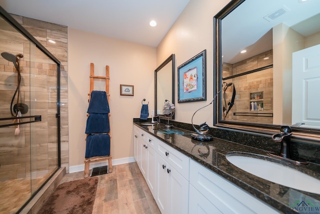 bathroom with double vanity, a stall shower, visible vents, wood finished floors, and a sink