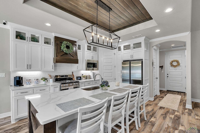 kitchen featuring pendant lighting, a kitchen island with sink, sink, appliances with stainless steel finishes, and white cabinetry