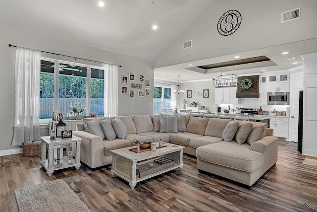 living room with a tray ceiling, dark wood-type flooring, a high ceiling, and an inviting chandelier