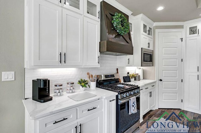 kitchen with white cabinets, light stone counters, premium range hood, and appliances with stainless steel finishes