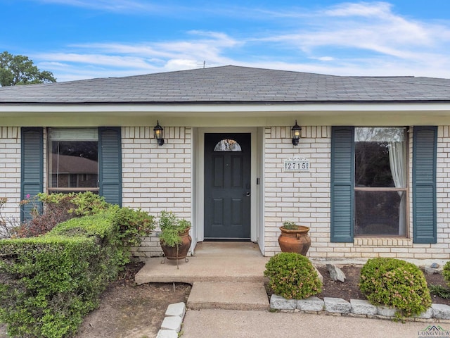 view of exterior entry featuring brick siding and roof with shingles
