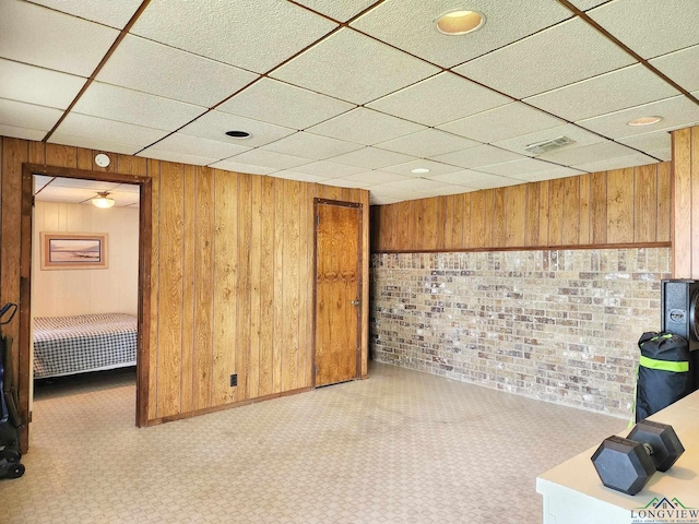 basement featuring a paneled ceiling, wooden walls, light carpet, and brick wall