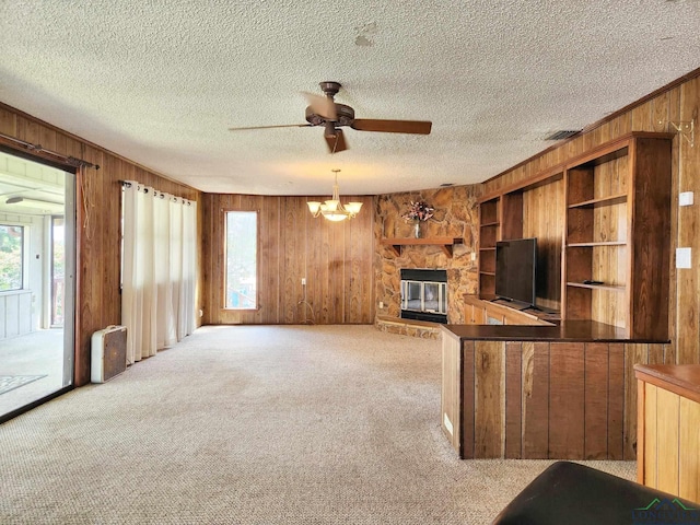 unfurnished living room with ceiling fan with notable chandelier, a fireplace, a wealth of natural light, and light carpet