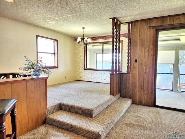 stairway featuring carpet flooring, an inviting chandelier, a healthy amount of sunlight, and wood walls