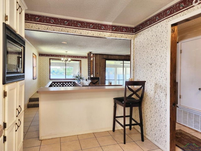 kitchen with black microwave, light tile patterned floors, a kitchen breakfast bar, crown molding, and white cabinets