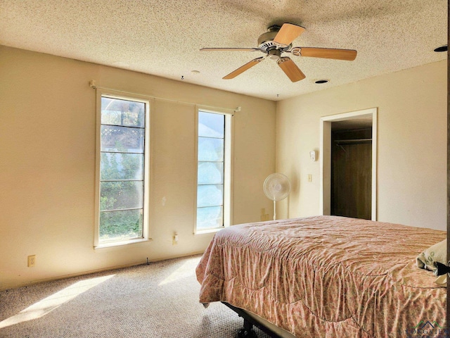 carpeted bedroom featuring a spacious closet, a closet, ceiling fan, and a textured ceiling