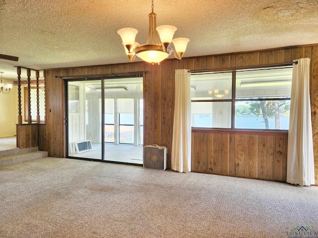 carpeted empty room with a wall mounted AC, wood walls, a textured ceiling, and an inviting chandelier