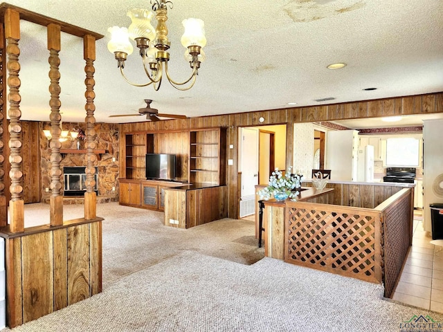 carpeted living room with a fireplace, a textured ceiling, ceiling fan with notable chandelier, and wood walls