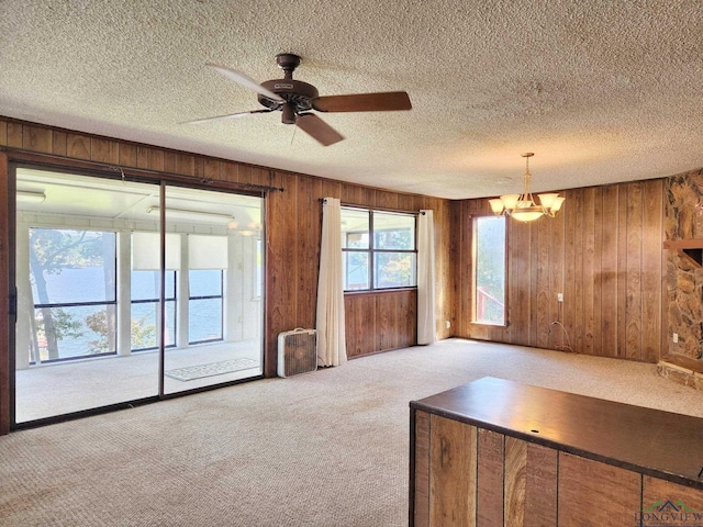 unfurnished living room with a textured ceiling, light carpet, wood walls, and ceiling fan with notable chandelier