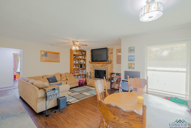 living room featuring crown molding, a ceiling fan, a brick fireplace, and wood finished floors