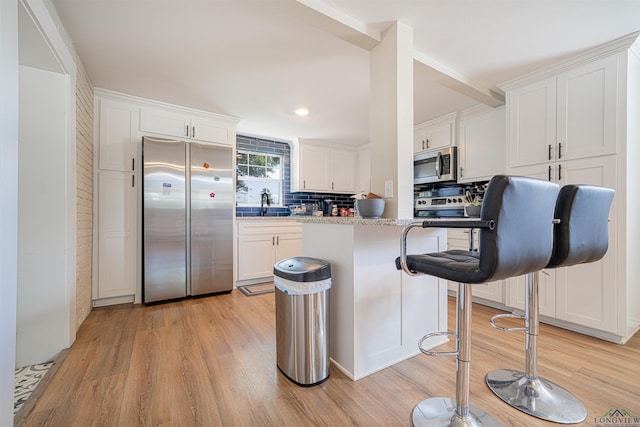 kitchen featuring appliances with stainless steel finishes, backsplash, light hardwood / wood-style flooring, white cabinets, and a breakfast bar area