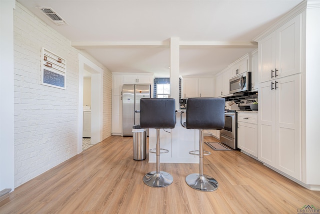 kitchen featuring stainless steel appliances, brick wall, light hardwood / wood-style floors, a breakfast bar area, and white cabinets