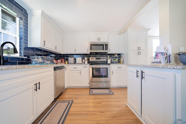 kitchen featuring white cabinetry, stainless steel appliances, tasteful backsplash, light stone counters, and light wood-type flooring