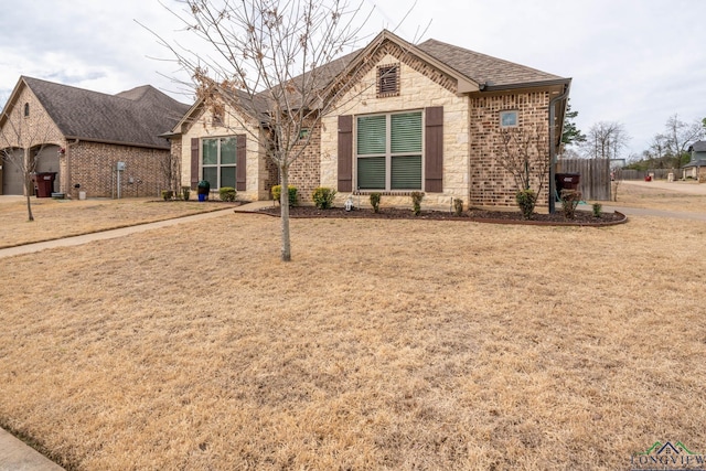 view of front of house featuring stone siding, brick siding, a front lawn, and roof with shingles