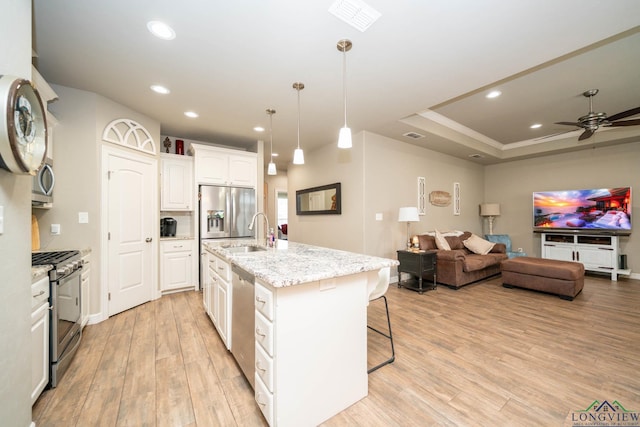 kitchen featuring stainless steel appliances, light wood-style floors, open floor plan, white cabinets, and a sink