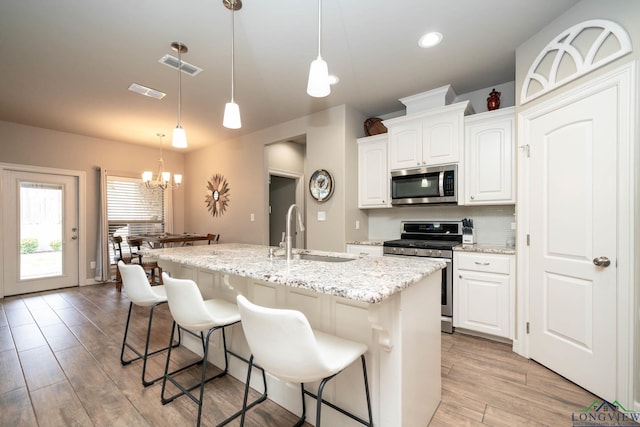 kitchen featuring visible vents, appliances with stainless steel finishes, a kitchen island with sink, a chandelier, and a sink