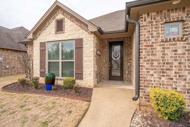 view of exterior entry featuring stone siding, roof with shingles, and brick siding