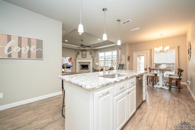 kitchen with light wood finished floors, visible vents, a tray ceiling, a fireplace, and stainless steel dishwasher