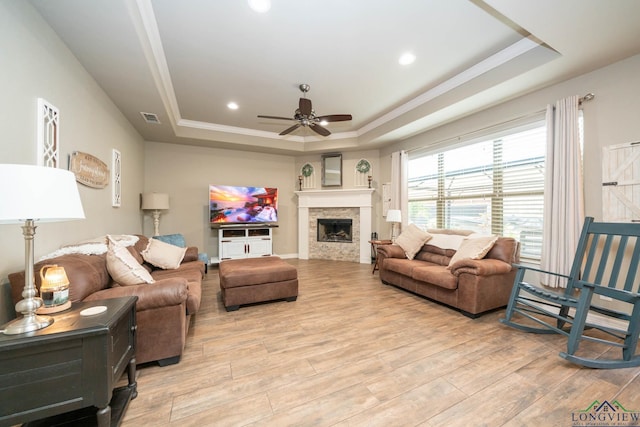 living area featuring a tray ceiling, a fireplace, light wood-style flooring, and ceiling fan