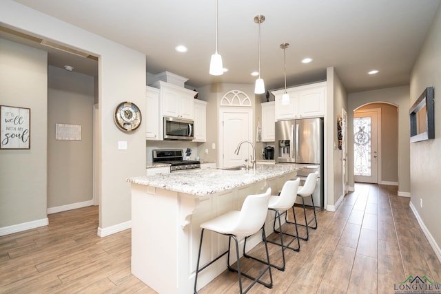 kitchen featuring light wood finished floors, arched walkways, white cabinets, appliances with stainless steel finishes, and a sink