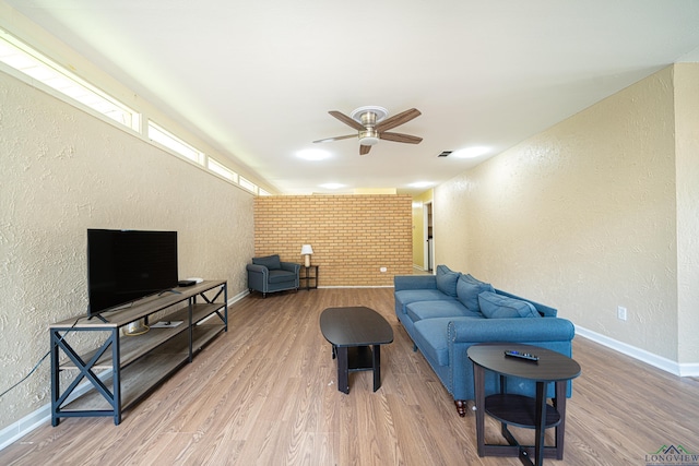 living room featuring ceiling fan, light hardwood / wood-style floors, and brick wall