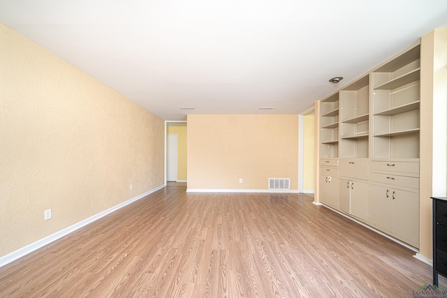 unfurnished living room featuring built in features and light wood-type flooring