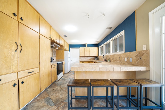 kitchen with tile countertops, white appliances, backsplash, kitchen peninsula, and a breakfast bar area