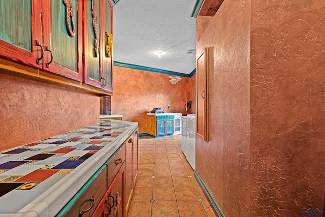 kitchen featuring light tile patterned floors, a textured wall, ornamental molding, a textured ceiling, and separate washer and dryer