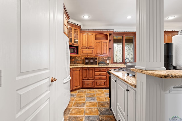 kitchen with light stone counters, backsplash, range, brown cabinetry, and glass insert cabinets