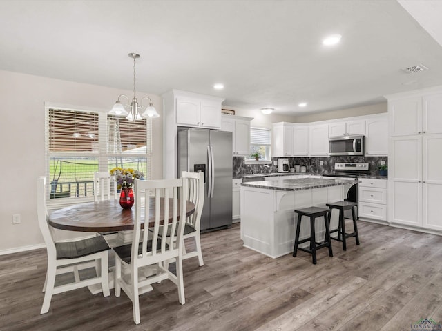 kitchen with a kitchen island, decorative backsplash, appliances with stainless steel finishes, an inviting chandelier, and white cabinetry