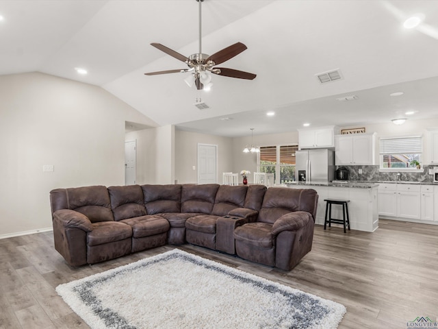 living area featuring lofted ceiling, ceiling fan with notable chandelier, visible vents, and light wood-type flooring