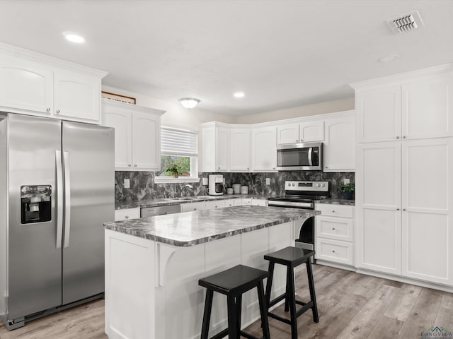 kitchen featuring white cabinetry, backsplash, light wood finished floors, and stainless steel appliances