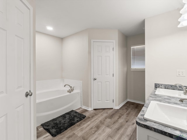 full bathroom featuring a bath, wood finished floors, baseboards, and a sink