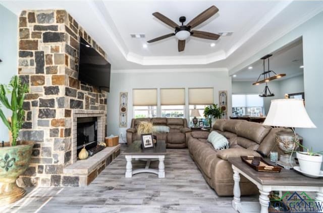 living room with light wood-type flooring, ornamental molding, a raised ceiling, ceiling fan, and a fireplace