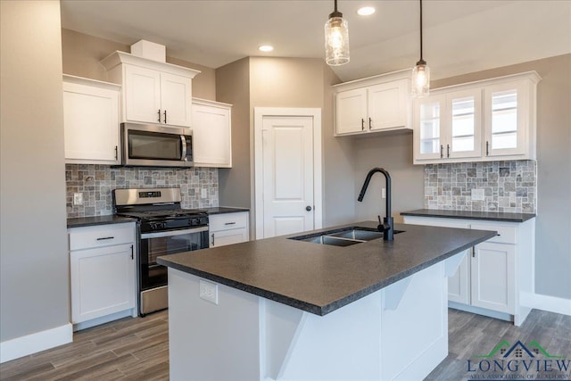 kitchen with sink, white cabinetry, hanging light fixtures, appliances with stainless steel finishes, and an island with sink