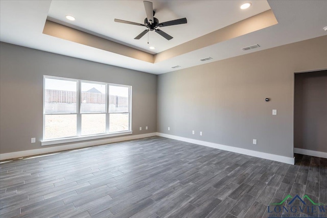 empty room featuring ceiling fan, dark hardwood / wood-style floors, and a tray ceiling